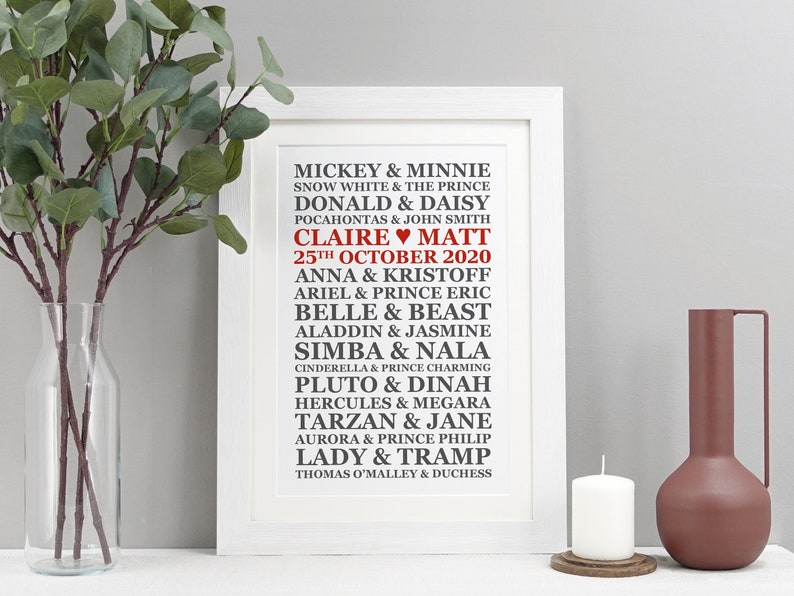May include: A white framed print with a black and red design featuring a list of Disney couples with their names and the date "25th October 2020" in red. The names "Claire" and "Matt" are also in red with a heart symbol between them.