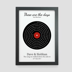 May include: A black and white framed print with a black vinyl record design. The record has the lyrics to the song "These Are The Days" by Van Morrison printed on it. The text "Dave & Siobhan" and "The song we walked down the aisle to 22nd July 2017" is printed below the record.