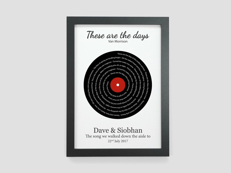 May include: A black and white framed print with a black vinyl record design. The record has the lyrics to the song "These Are The Days" by Van Morrison printed on it. The text "Dave & Siobhan" and "The song we walked down the aisle to 22nd July 2017" is printed below the record.