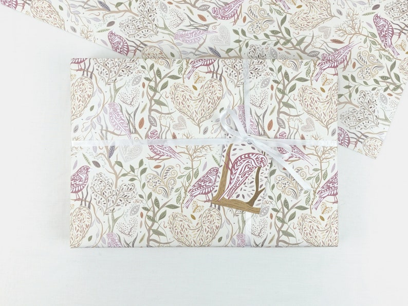 May include: White gift wrap with a repeating pattern of stylised birds, leaves, and hearts in shades of pink, brown, and green.