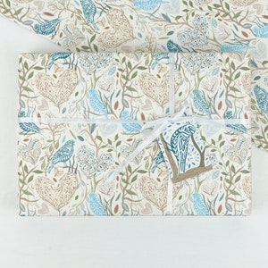 May include: A white gift box wrapped in blue and brown patterned paper with a white ribbon and a blue and brown bird tag. The paper features a repeating pattern of birds, leaves, and branches.