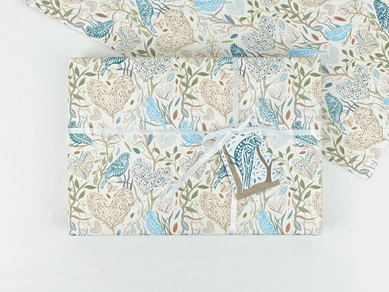 May include: A white gift box wrapped in blue and brown patterned paper with a white ribbon and a blue and brown bird tag. The paper features a repeating pattern of birds, leaves, and branches.