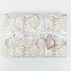 May include: A white gift box with a white ribbon and a brown tag. The box is wrapped in paper with a pattern of birds, leaves, and hearts in shades of pink, brown, and green.