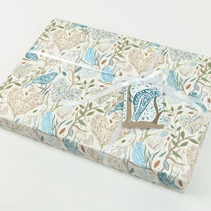 May include: A gift box wrapped in white paper with a blue and brown bird pattern. The box is tied with a white ribbon and has a small blue and brown bird tag attached.