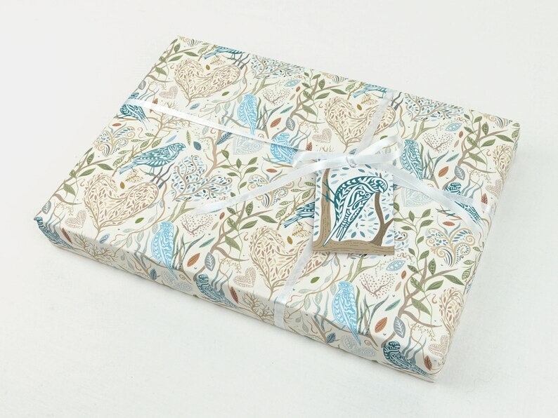 May include: A gift box wrapped in white paper with a blue and brown bird pattern. The box is tied with a white ribbon and has a small blue and brown bird tag attached.