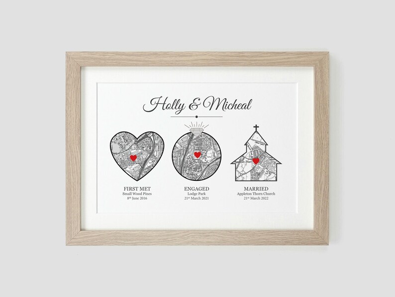 May include: A black and white map print with red hearts marking locations. The print is framed in a light wood frame and includes the text "Holly & Micheal", "First Met", "Engaged", and "Married" with corresponding dates.