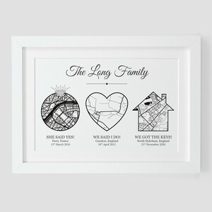 May include: A black and white print with the text "The Long Family" at the top. The print features three maps: a ring, a heart, and a house. Each map is labeled with a date and location. The ring map is labeled "She said yes!" with the date "15th March 2000" and the location "Paris, France". The heart map is labeled "We said I do!" with the date "18th April 2002" and the location "Caunton, England". The house map is labeled "We got the keys!" with the date "23rd November 2020" and the location "North Hykcham, England".