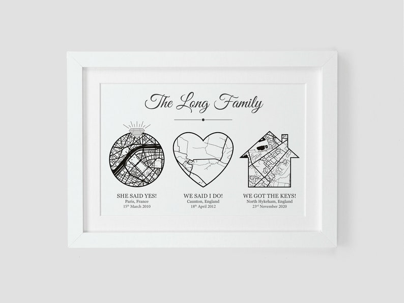 May include: A black and white print with the text "The Long Family" at the top. The print features three maps: a ring, a heart, and a house. Each map is labeled with a date and location. The ring map is labeled "She said yes!" with the date "15th March 2000" and the location "Paris, France". The heart map is labeled "We said I do!" with the date "18th April 2002" and the location "Caunton, England". The house map is labeled "We got the keys!" with the date "23rd November 2020" and the location "North Hykcham, England".