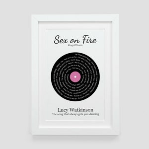 May include: A black and white framed print with a pink circle in the center. The print features a black vinyl record with the song lyrics for "Sex on Fire" by Kings of Leon. The text "Lucy Watkinson" and "The song that always gets you dancing" are printed below the record.