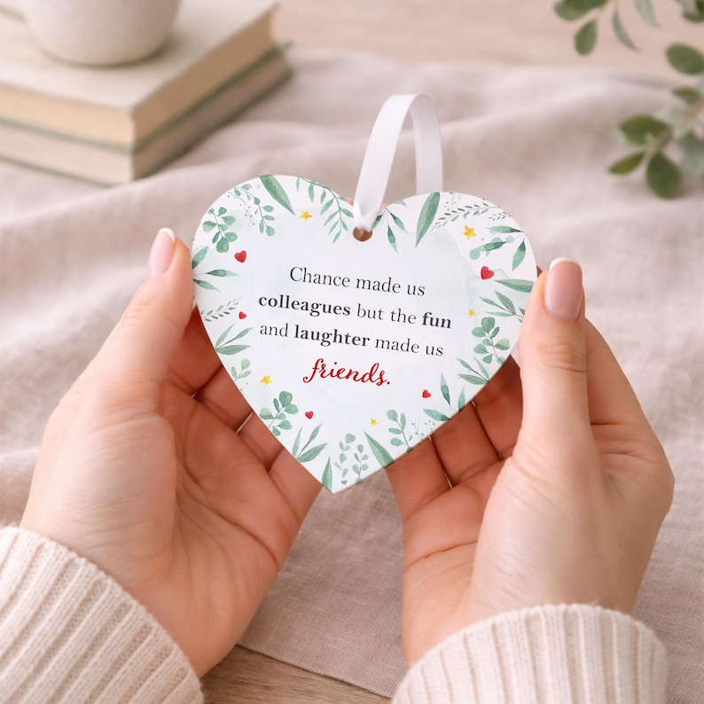 K&ouml;nnte beinhalten: Herzf&ouml;rmiger Anh&auml;nger mit wei&szlig;em Band. Das Ornament hat ein Blumendesign und den Text "Chance made us colleagues but the fun and laughter made us friends." in Schwarz und Rot.