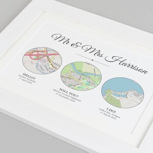 May include: A white framed print with three circular maps representing different locations. The text "Mr & Mrs Harrison" is at the top of the print. The maps are labeled "HELLO! Neschey, Rochdale 1st April 2018", "WILL YOU? Melrose, Scottish Highlands 3rd November 2020", and "I DO! Galley Bay, Antigua 1st March 2022".