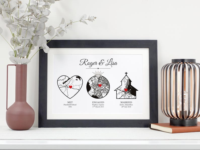 May include: A black and white print with a map of three locations, labeled "Met", "Engaged", and "Married". The locations are marked with red hearts. The print is framed in black and has the names "Roger & Lisa" at the top.