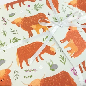 May include: A light green wrapping paper with a repeating pattern of brown Highland cows and white flowers. The cows are in various poses, some with calves. A white ribbon is tied around the paper with a tag.