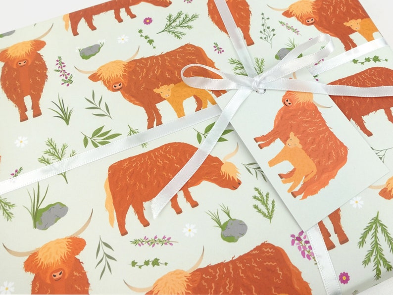 May include: A light green wrapping paper with a repeating pattern of brown Highland cows and white flowers. The cows are in various poses, some with calves. A white ribbon is tied around the paper with a tag.