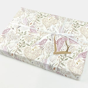 May include: A white gift box with a floral and bird pattern. The box is wrapped with a white ribbon and has a small tag with a bird design.