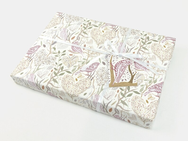 May include: A white gift box with a floral and bird pattern. The box is wrapped with a white ribbon and has a small tag with a bird design.