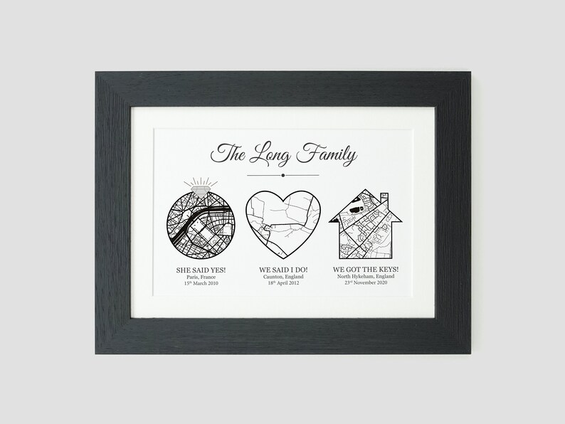 May include: A black and white print with the text "The Long Family" at the top. The print features three maps: a circle with a diamond ring, a heart, and a house. Each map is labeled with a location and date. The text below the maps reads "She said yes! Paris, France 15 March 2010", "We said I do! Caunton, England 18 April 2002", and "We got the keys! North Hykeham, England 23 November 2020".