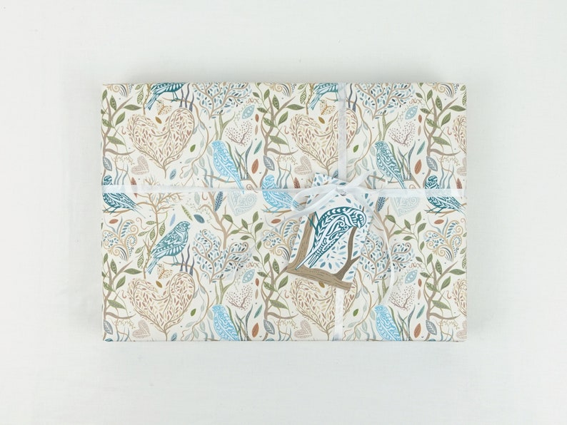 May include: White gift wrap with a blue and brown bird and leaf pattern. The gift is tied with a white ribbon and a blue and brown bird tag.