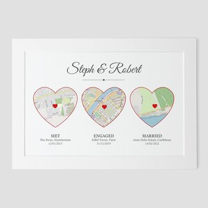 Pu&ograve; includere: Un biglietto bianco con una mappa di tre luoghi a forma di cuore. Il testo "Steph & Robert" &egrave; in cima al biglietto. Il testo "MET" &egrave; sotto il primo cuore, "ENGAGED" &egrave; sotto il secondo cuore e "MARRIED" &egrave; sotto il terzo cuore. Le date di ogni evento sono elencate sotto i nomi dei luoghi.