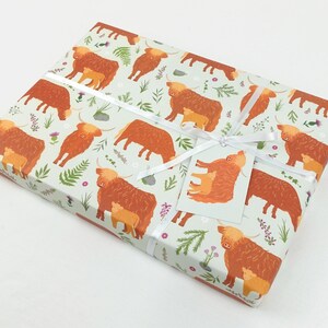 May include: Gift wrap featuring a repeating pattern of brown Highland cows with calves on a light green background with small flowers and leaves.