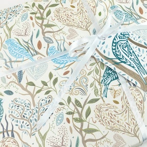 May include: White gift wrap with a blue and brown patterned design featuring birds, leaves, and branches. A white ribbon is tied around the package with a blue and brown gift tag attached.