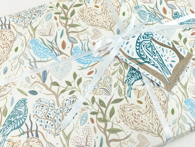 May include: White gift wrap with a blue and brown patterned design featuring birds, leaves, and branches. A white ribbon is tied around the package with a blue and brown gift tag attached.