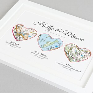 Pu&ograve; includere: Una stampa incorniciata bianca con tre cuori rossi, ognuno contenente una mappa di una posizione diversa. Il testo "Holly & Mason" &egrave; in cima alla stampa. Il testo sotto ogni cuore recita "HELLO! The Ship, High Newton 1 giugno 2018", "WILL YOU... Belle Isle, Windermere 15 giugno 2019", e "I DO! Hampsfield House, Hampsfield 28 giugno 2022".