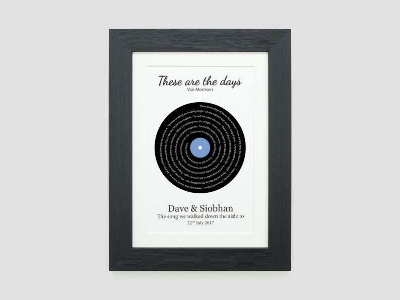 May include: A black and white framed print with a black vinyl record design. The record has the lyrics to the song "These Are The Days" by Van Morrison printed on it. The text below the record reads "Dave & Siobhan, The song we walked down the aisle to, 22 July 2017."