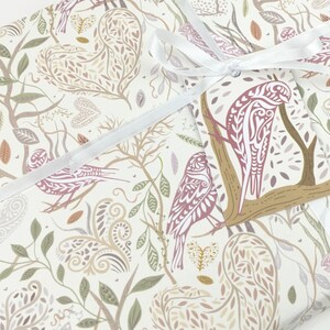 May include: White wrapping paper with a repeating pattern of stylised birds, leaves, and hearts in shades of brown, pink, and green. A white ribbon is tied around the paper with a gift tag featuring a brown branch with a pink bird.