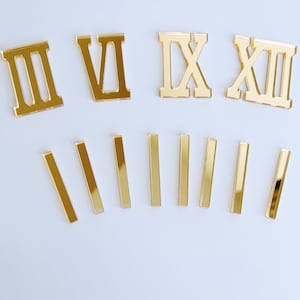 May include: Gold Roman numeral clock numbers, including I, II, III, VI, IX, X, XII, and seven gold stick numbers. These numbers are used for a DIY clock project.