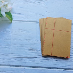 May include: A stack of clear acrylic sheets with protective brown paper backing. The paper has red markings and numbers.