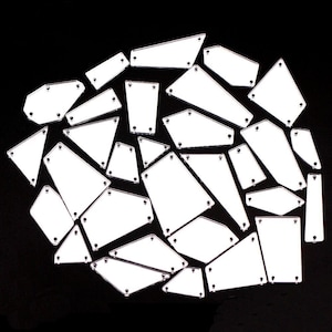 Puede incluir: Una colección de piedras de cristal de acrílico transparentes y facetadas en varias formas geométricas. Las piedras de cristal están esparcidas sobre un fondo negro.