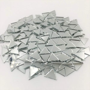 May include: A pile of silver triangular mirror tiles. The tiles are small and have a reflective surface.