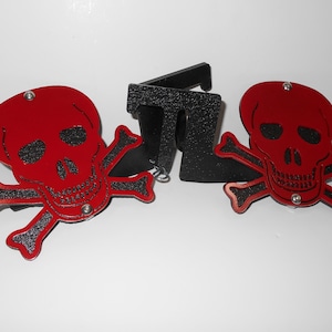 May include: Two red and black skull and crossbones decorations. The skulls are red with black eye sockets and a black mouth. The crossbones are black with a red outline.