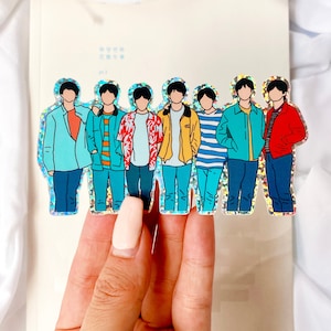 May include: A holographic sticker featuring a group of seven cartoon figures wearing colorful clothing. The figures are standing in a line, and each figure has a different hairstyle and facial expression. The sticker is on a white background.