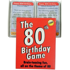 May include: A red box with the text "The 80th Birthday Game" in white. The box has a smaller white box on the front with the text "New" in a red circle. The text "Brain-teasing fun, all on the theme of 80" is printed in white at the bottom of the box.