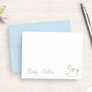 May include: A white card with a light blue envelope. The card has a rocking horse illustration and the text "Baby Dillon".