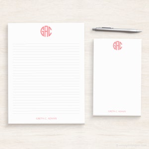 May include: Two white lined notepads with pink monogrammed initials "GAC" in a circle. The larger notepad has the name "Greta C. Adams" printed at the bottom. The smaller notepad has the name "Greta C. Adams" printed at the bottom right corner.