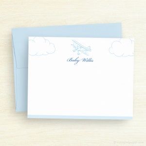 May include: A white baby shower stationery card with a blue airplane and clouds. The text "Baby Willis" is printed in blue cursive.