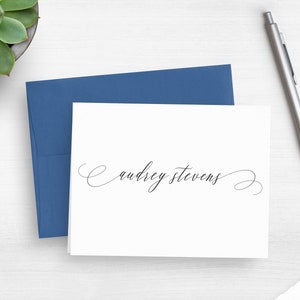 May include: A white card with a blue envelope. The card has the name "Audrey Stevens" written in elegant cursive script.