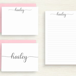 May include: White stationery set featuring the name "hailey" in elegant black script. Includes notecards with pink envelopes and a lined notepad. The set is designed for personalized correspondence.