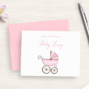 May include: A white card with pink text that reads "From the nursery of Baby Lucy". A pink and white baby carriage with brown wheels is illustrated on the card.