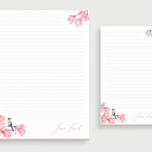 May include: Two lined notepads with pink magnolia flowers and a blue bird on the bottom corner. The notepad on the left has the name "Jane Finch" written in cursive at the bottom. The notepad on the right has the name "Jane Finch" written in cursive at the bottom right corner.
