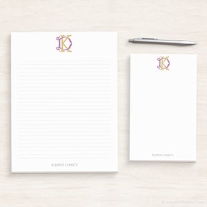 May include: Two white lined notepads with a gold and purple monogram of the letters "KD". The notepad on the left has the name "Karen Darcy" printed at the bottom. The notepad on the right has the name "Karen Darcy" printed at the bottom.