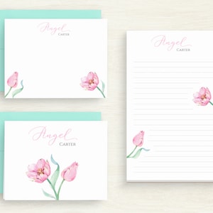 May include: Two white note cards with a light blue envelope. The note cards feature pink watercolour tulips and the text "Angel Carter".