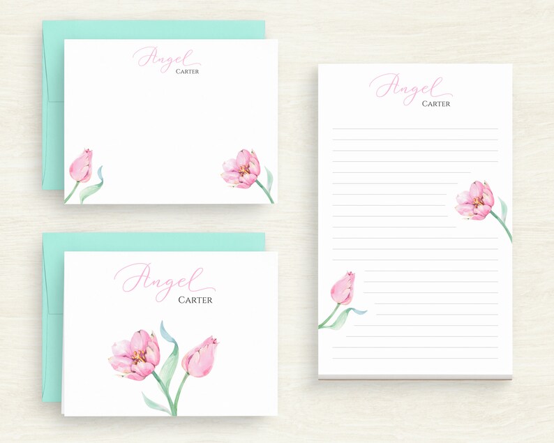 May include: Two white note cards with a light blue envelope. The note cards feature pink watercolour tulips and the text "Angel Carter".