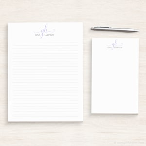 May include: Two white notepad sets with lined paper. The top of each notepad has a purple monogram with the initials "GH" and the name "Gina Hampton".