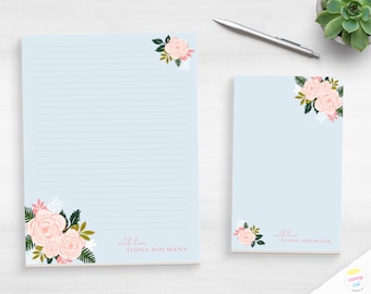 May include: A light blue stationery set featuring a large lined sheet and a smaller notepad, both decorated with pink rose illustrations and green foliage. The text "with love FIONA HOLMANN" is printed in pink on the bottom right of each sheet.