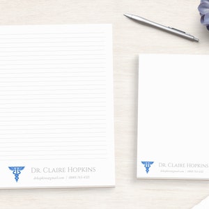 May include: Two white lined notepad sets with a blue medical caduceus symbol and the text "DR. CLAIRE HOPKINS" and contact information.