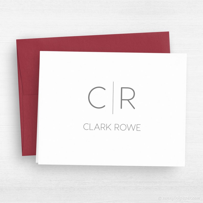 May include: White card with a gray monogram of "C|R" and the text "CLARK ROWE" below. The card is sitting on a red envelope.